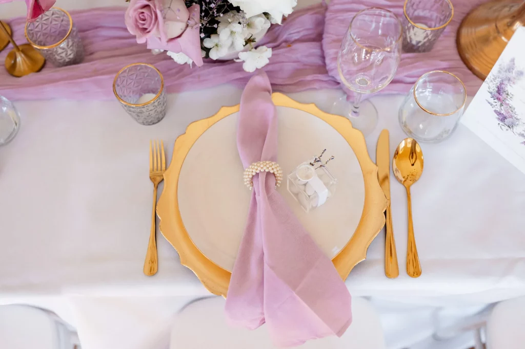 gedeckter hochzeitstisch mit goldbesteck und rosa serviette