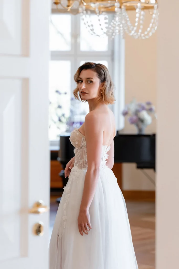 Braut im weißen Kleid vor Fenster und Klavier