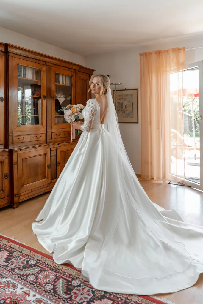 A beautiful bride stands in a room with a bouquet and a beautiful dress