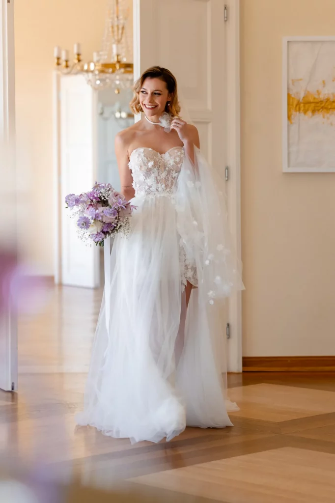 Lächelnde Braut mit Spitzenkleid und Blumenstrauß