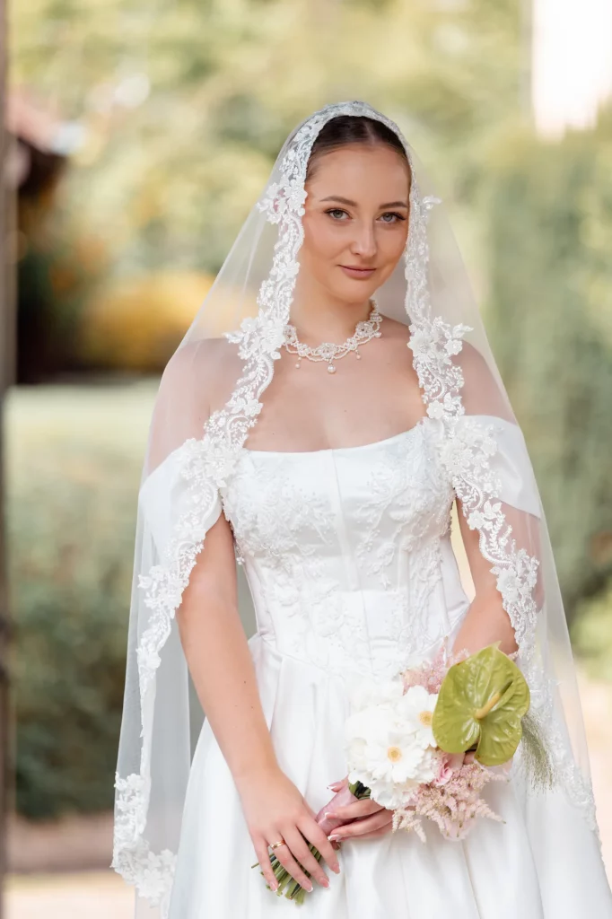 Braut mit besticktem Schleier und Blumenstrauß