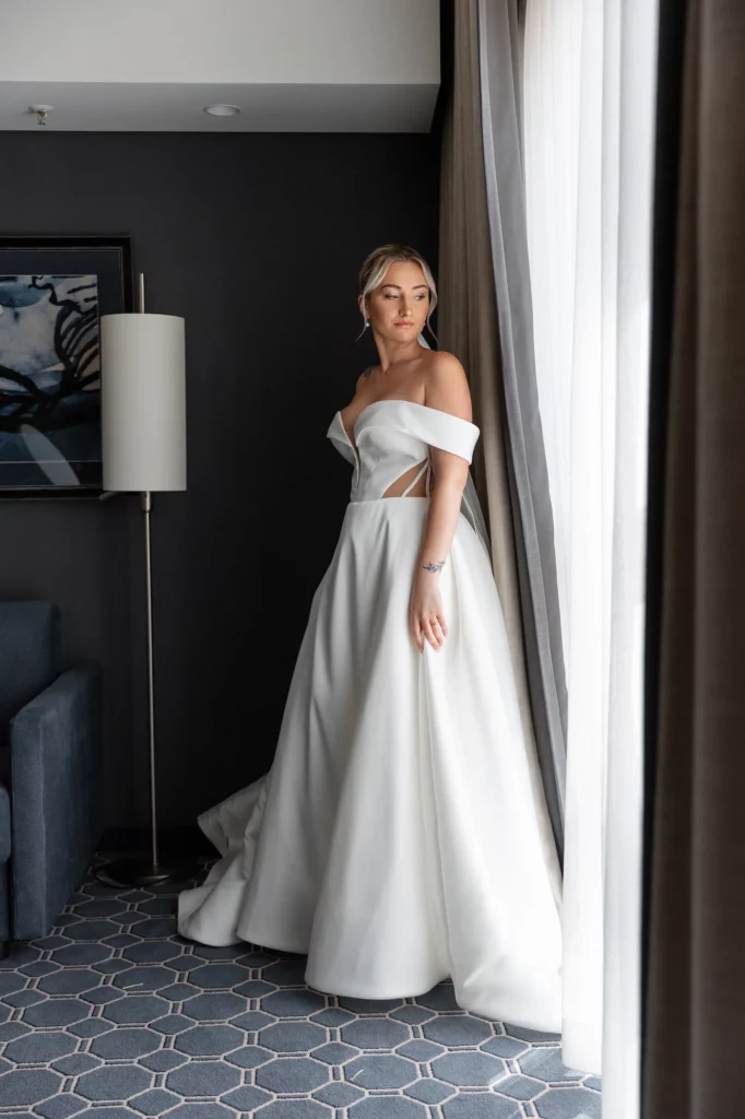 Braut im weißen Kleid blickt aus Fenster