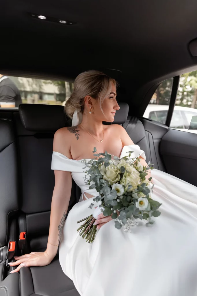 Braut im weißen Kleid mit Blumenstrauß sitzt im Auto