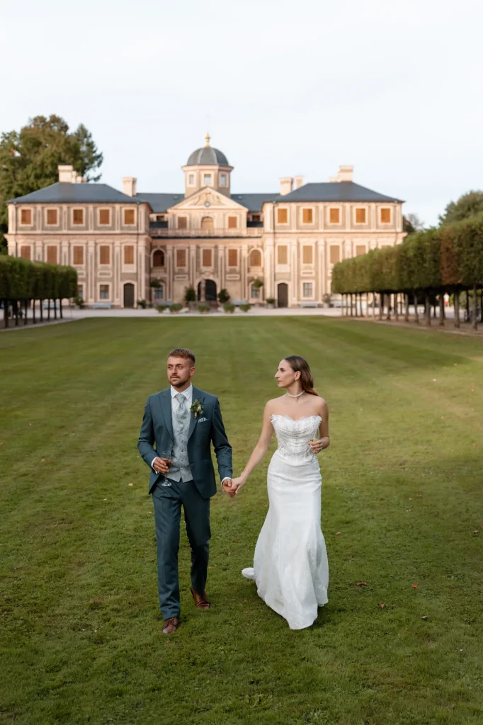 Brautpaar hält Händchen auf Rasen vor Schloss