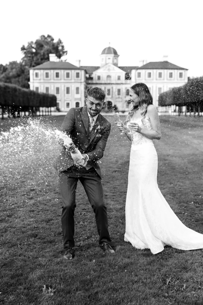 Brautpaar öffnet Sektflasche vor Schloss