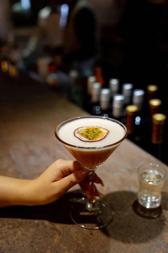 Hand hält Cocktail mit Passionsfrucht auf Theke