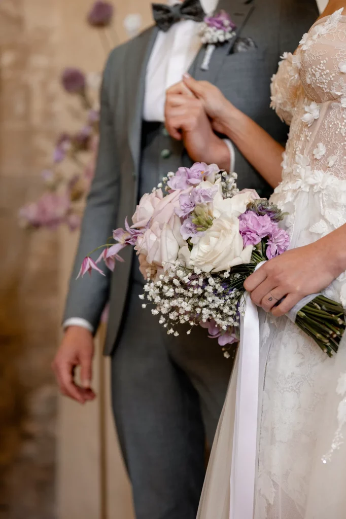 Braut hält zarten Brautstrauß mit weißen und lila Blumen