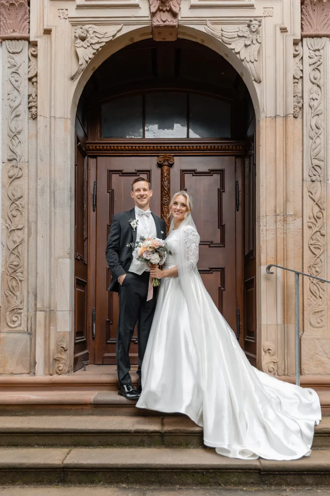 The wedding couple stands near the church doors