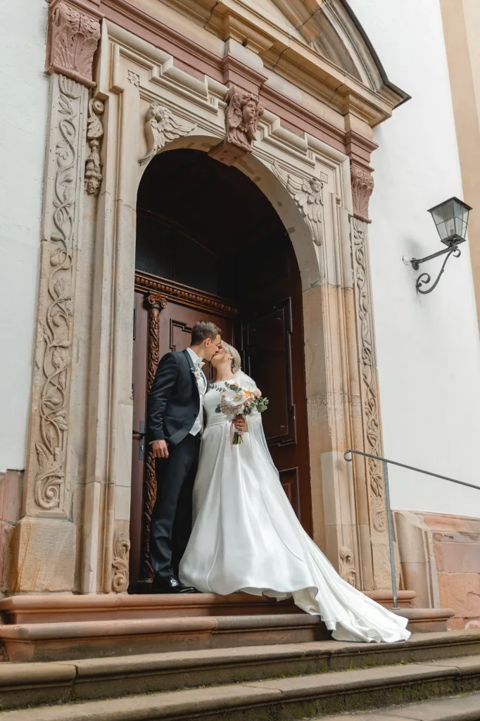 The wedding couple stands near the church doors, they are kissing