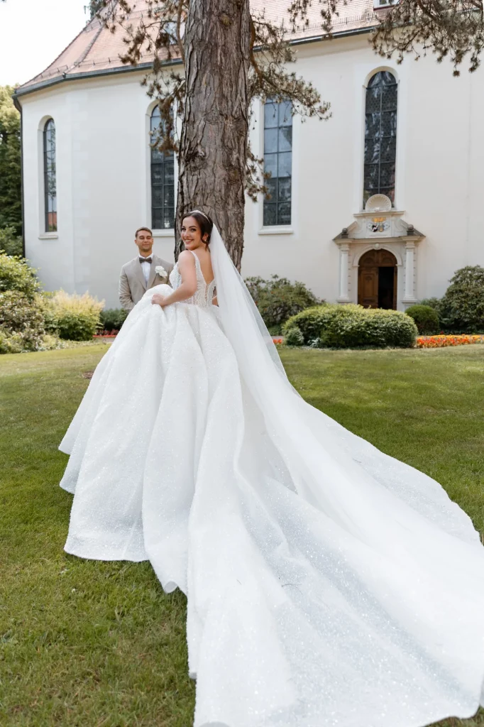 Braut im weißen Kleid vor Bräutigam und Kirche