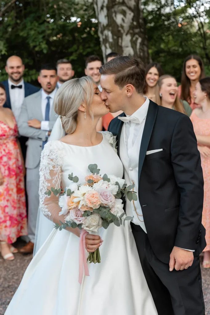 a wedding couple kisses with their friends in the background