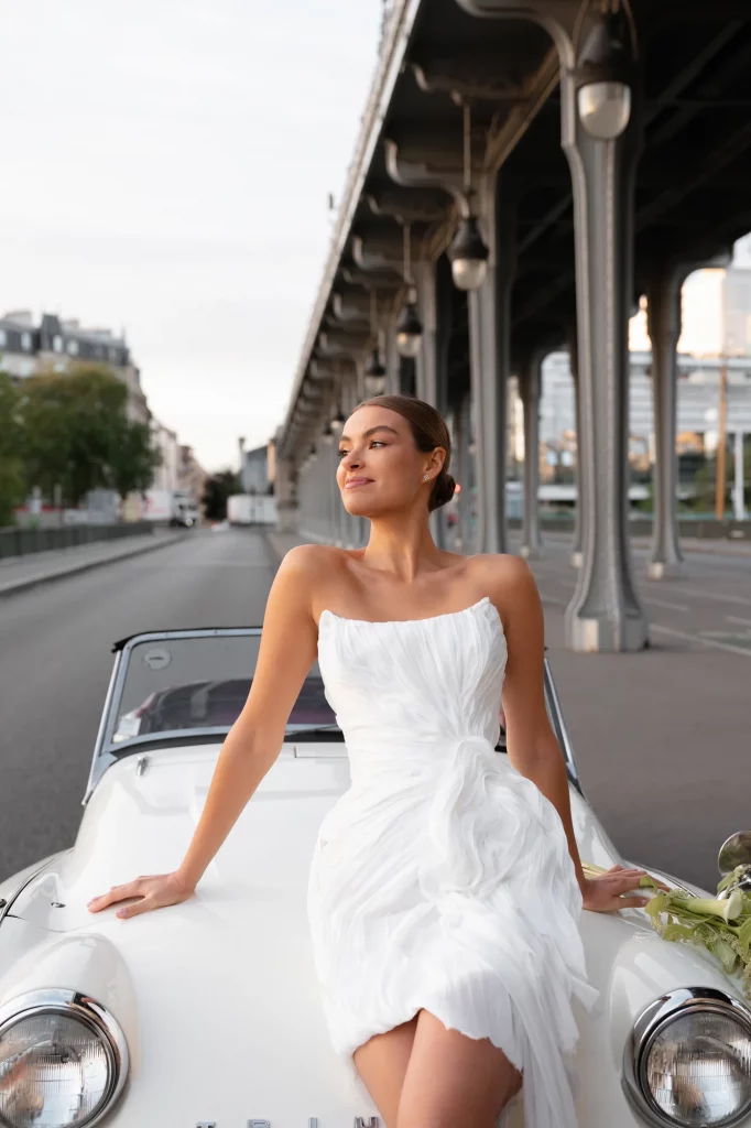 Frau in weißem Kleid sitzt auf der Motorhaube eines weißen Autos