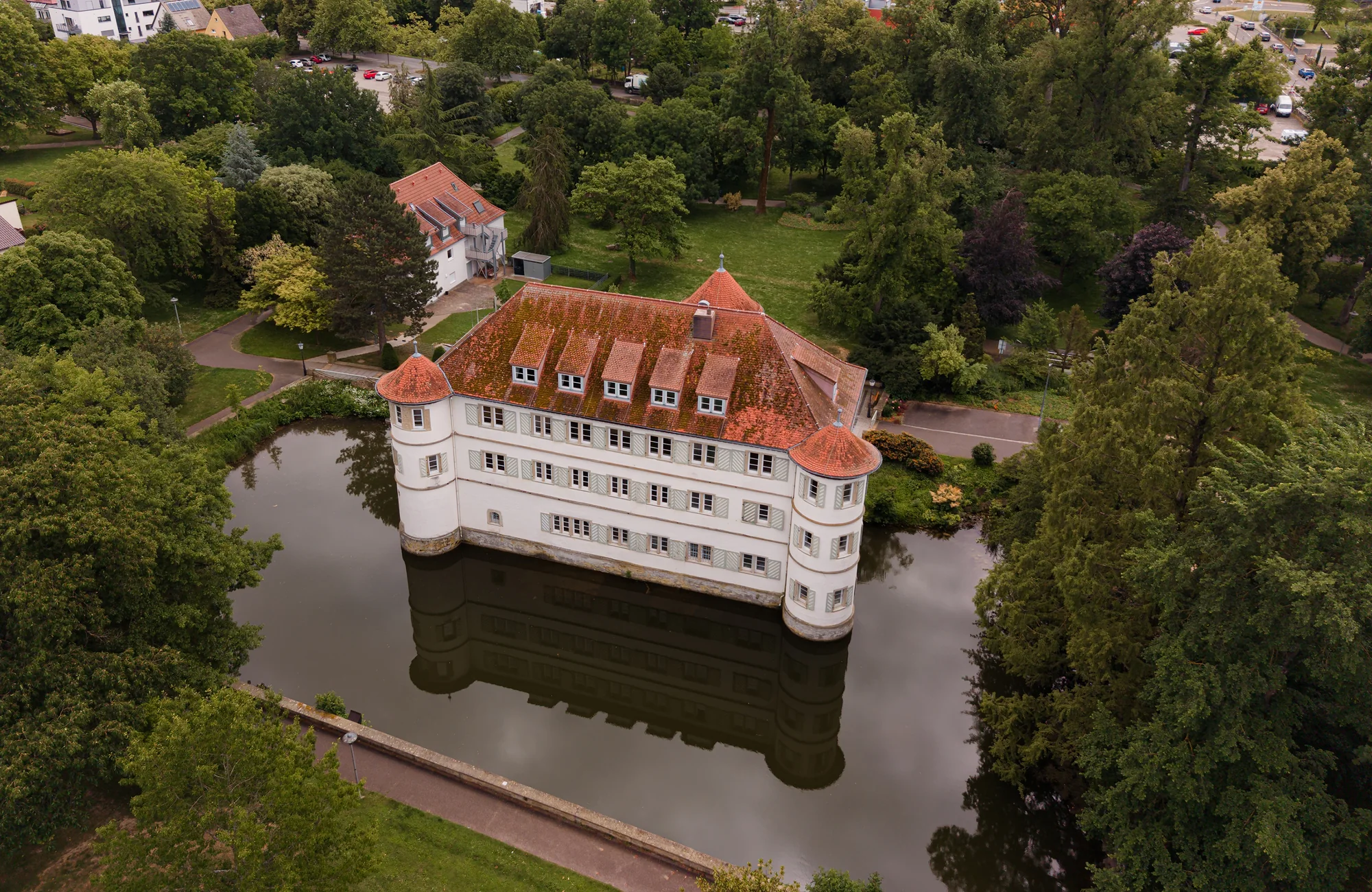 ein großes weißes gebäude mit roten dachziegeln umgeben von wasser und bäumen