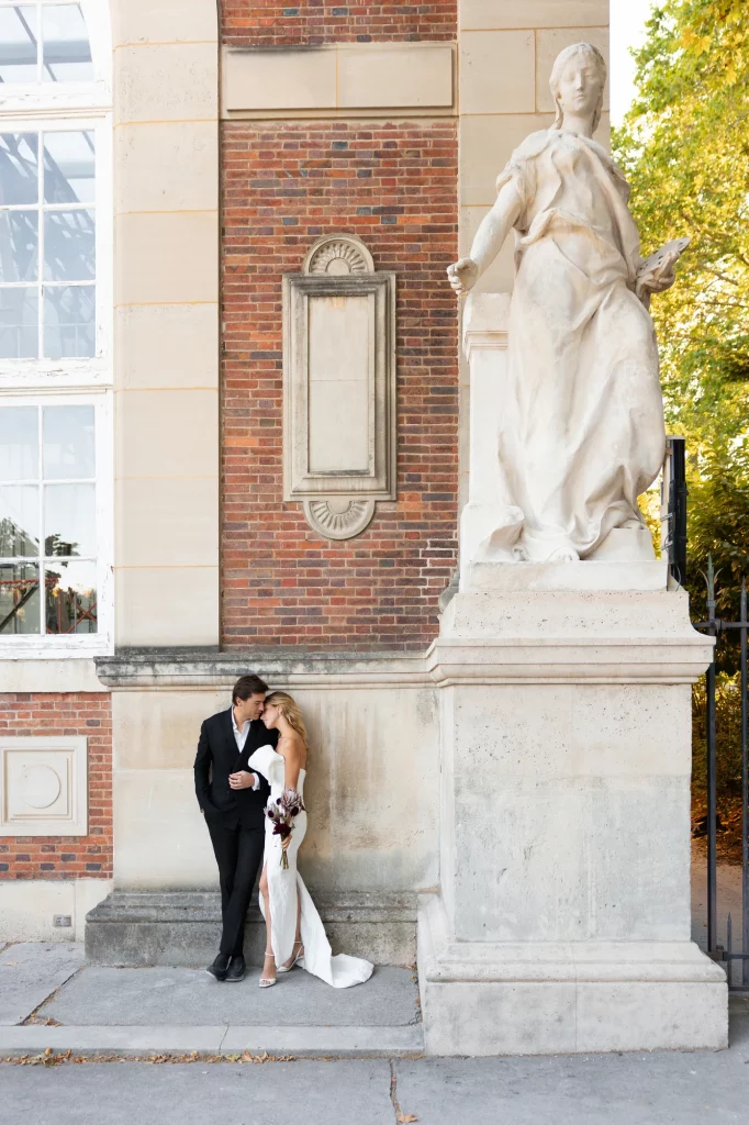 Zwei Personen stehen eng beieinander vor einer Statue und einer Backsteinfassade