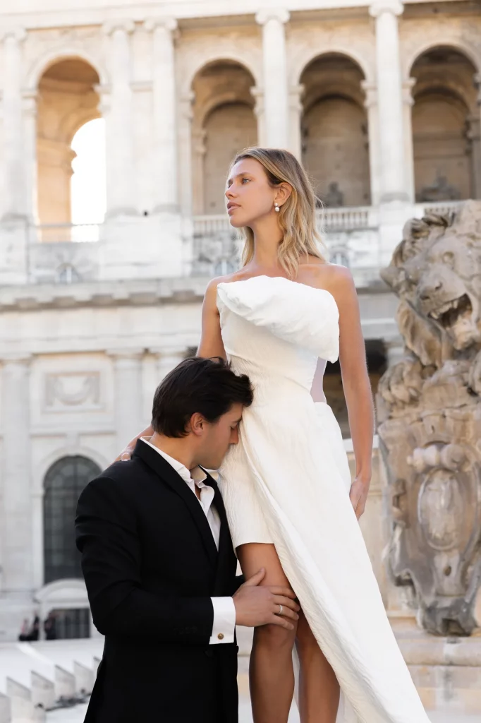 Zwei Personen vor hellen Säulen, eine trägt ein weißes Kleid und die andere einen schwarzen Anzug.