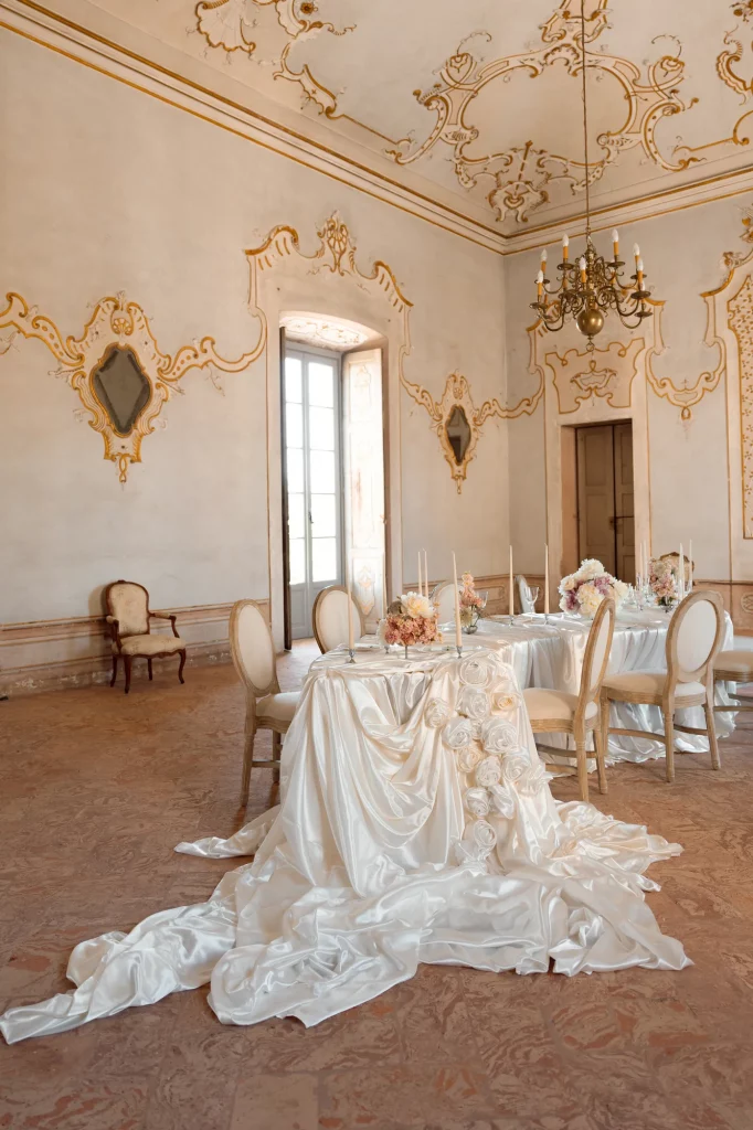 ein Tisch mit weißem Satin-Tuch und Blumenarrangements in einem eleganten Raum