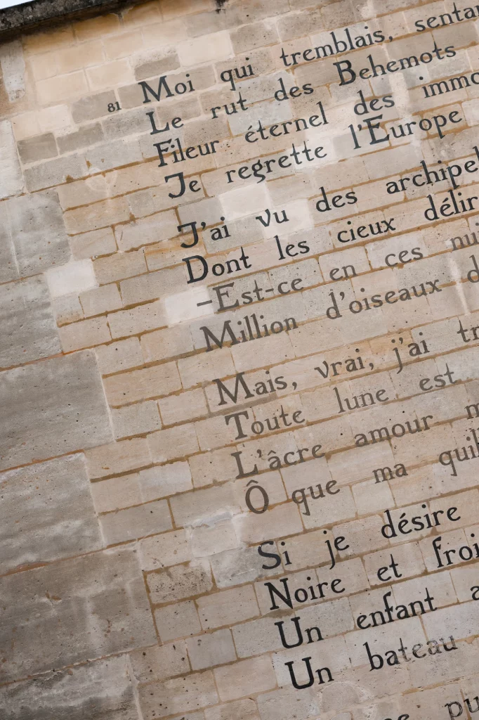 Große dunkle Buchstaben stehen auf einer hellen Wand aus Steinblöcken.