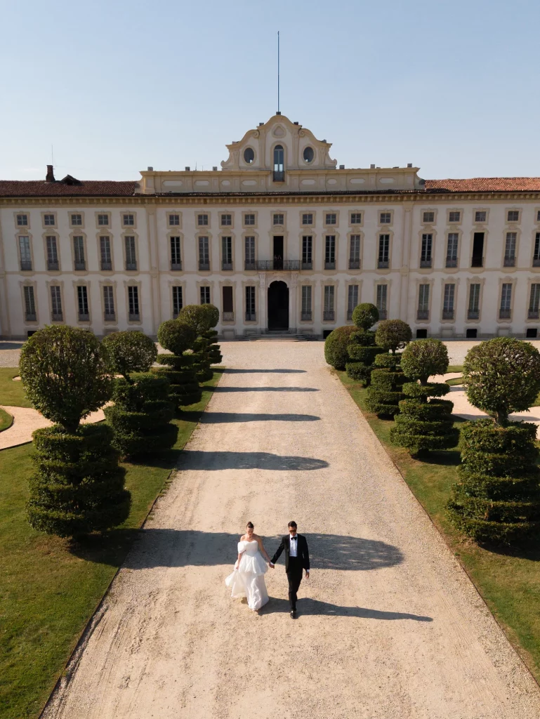 Ein Paar in formeller Kleidung geht auf einem Weg vor einem großen historischen Gebäude
